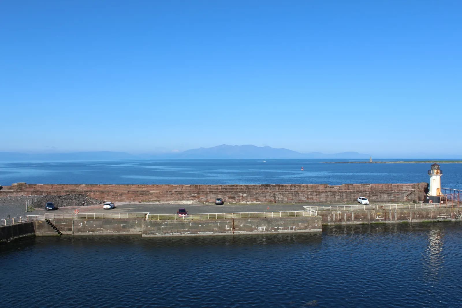 Ardrossan harbour wall and lighthouse, with Arran on the horizon across a calm blue sea
