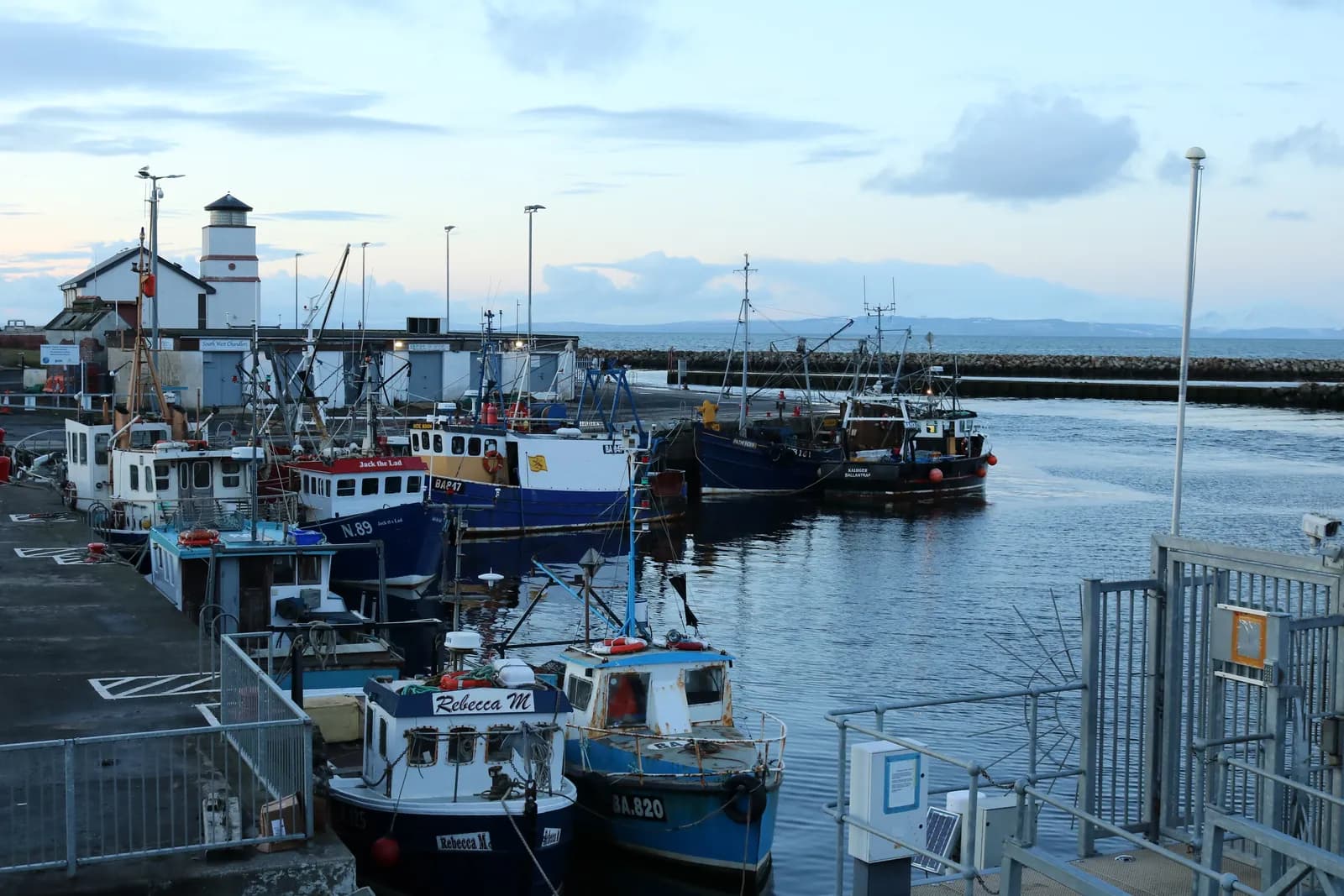 Fishing boats moored in Girvan harbour, with the harbour lighthouse and the sea beyond