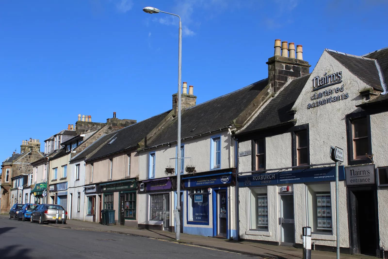 A row of shops and offices where High Street meets Main Street in Stewarton, under a clear blue sky