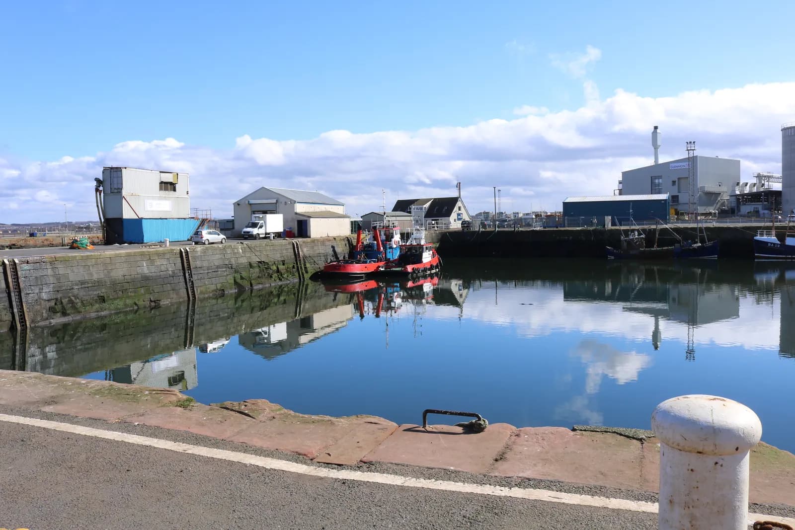 Tugs moored in Troon's inner harbour, with the quayside buildings reflected in still water